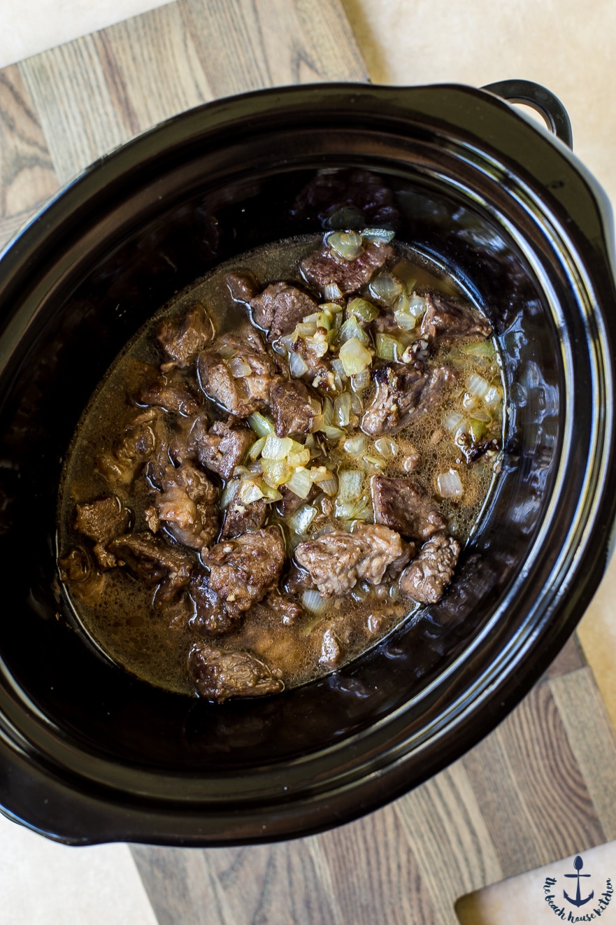 Overhead photo of beef cubes and onions in slow cooker