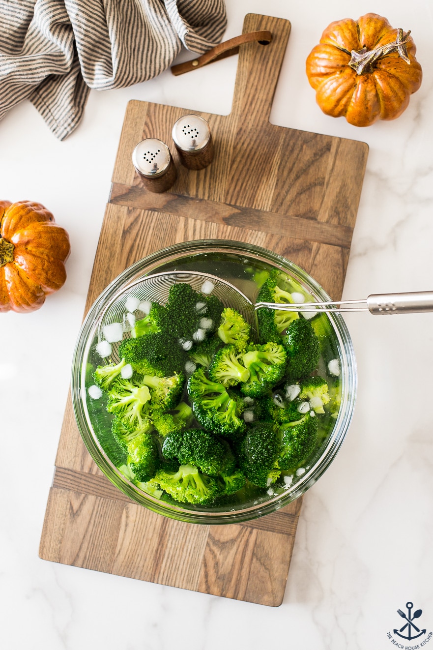 Overhead photo of bowl filled with broccoli, ice and water on a wooden board