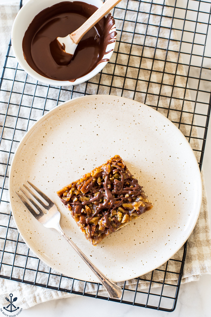 Overhead photo of a chocolate drizzled maple pecan bar on a plate with a fork