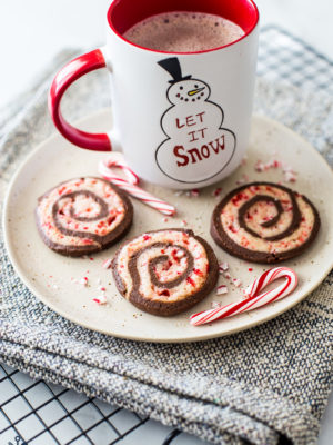 Chocolate peppermint pinwheel cookies on a plate with a mug of hot cocoa