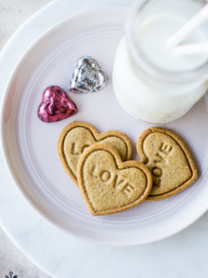 Overhead photo of 3 heart shaped cookies imprinted with LOVE on a plate with a bottle of milk