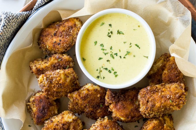 Overhead photo of pretzel crusted chicken nuggets with mustard dipping sauce on a tray on a wooden board