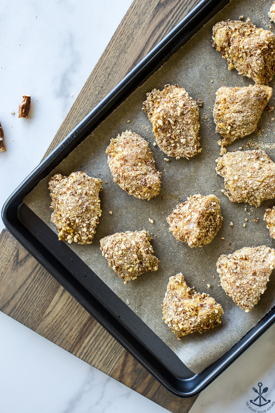 Overhead photo of pre-baked pretzel crusted chicken nuggets on a baking sheey lined with parchment paper