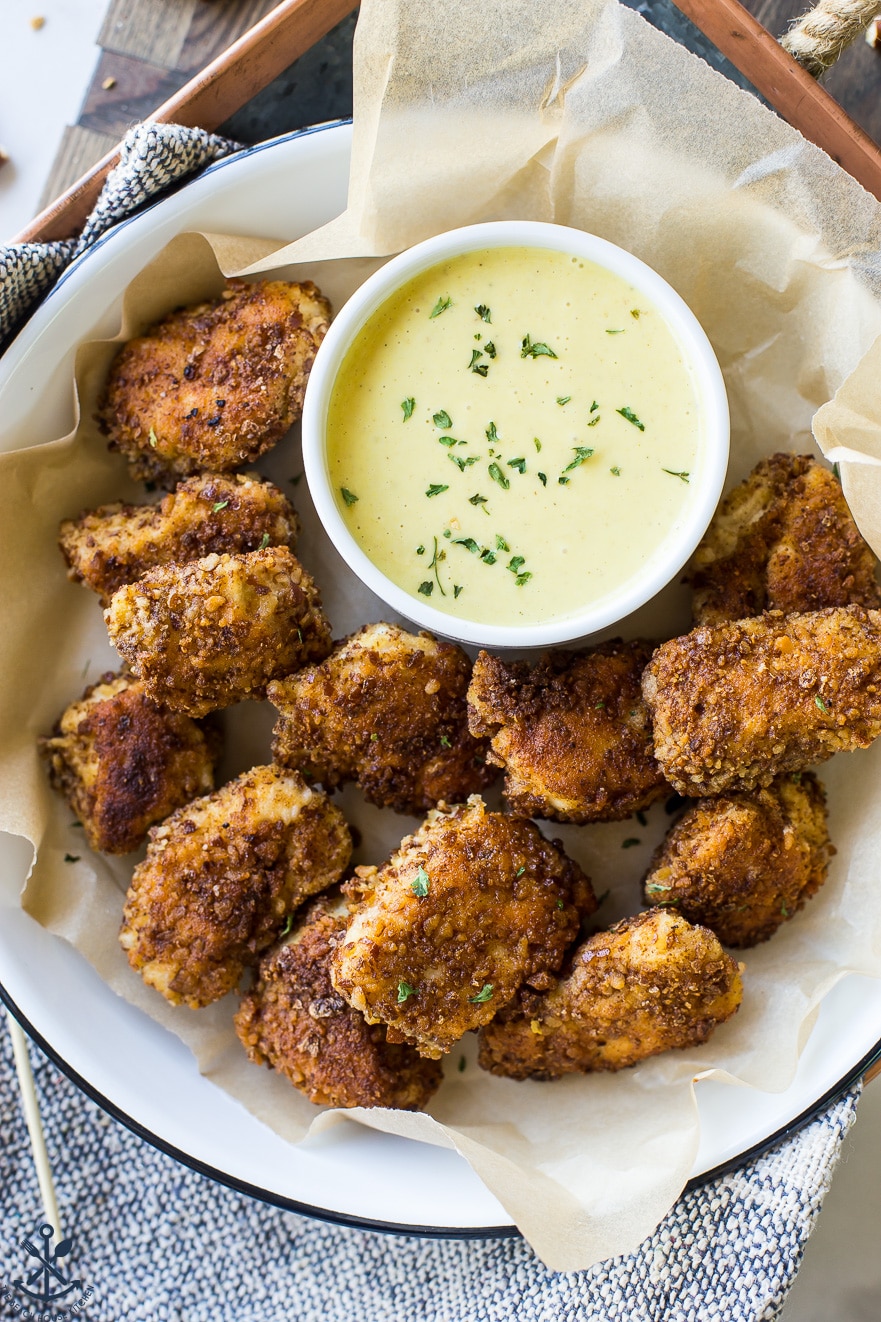 Overhead photo of pretzel crusted chicken nuggets with mustard dipping sauce on a tray on a wooden board