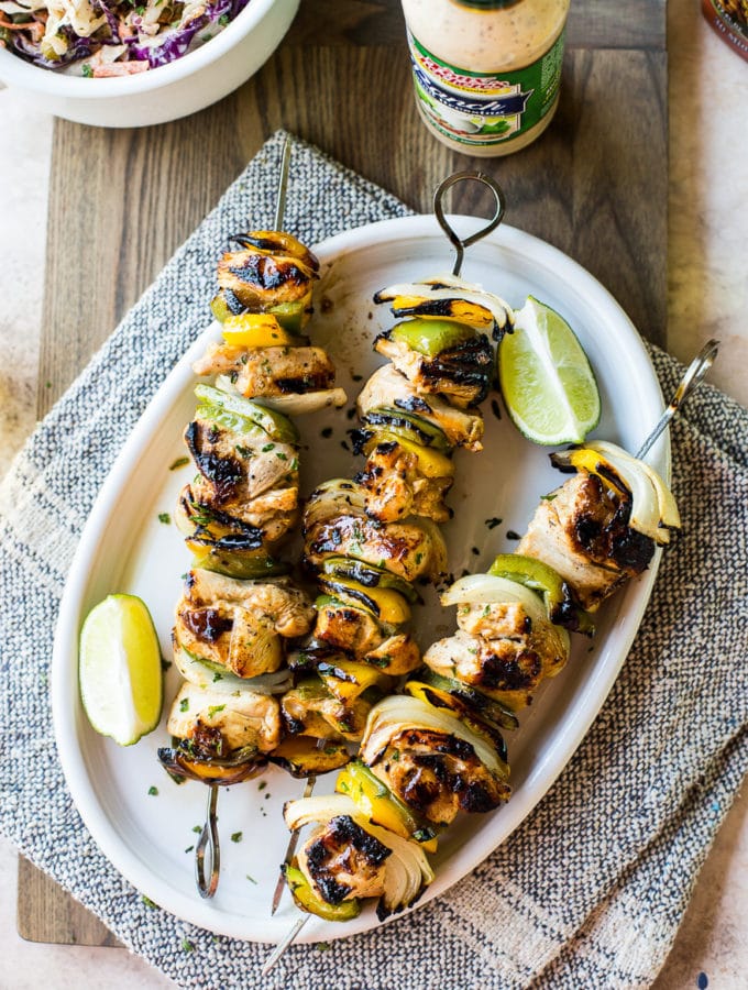Overhead photo of chicken skewers on a white oval plate on a wooden board