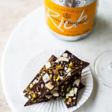 Chocolate coconut pistachio bark on a round marble board with a bottle of champagne