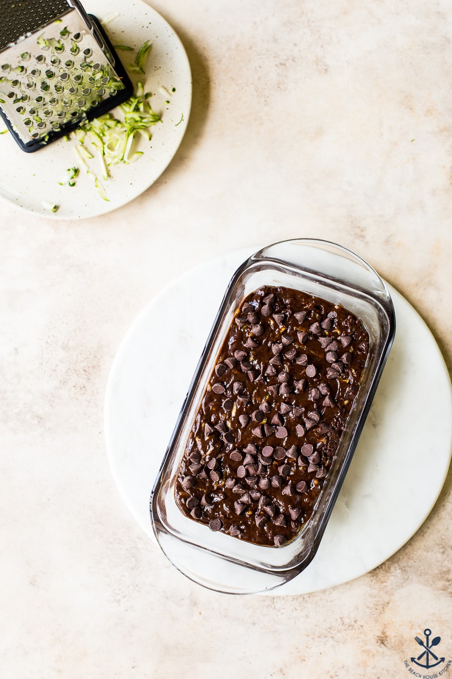 Overhead photo of pre-baked chocolate zucchini bread in glass loaf pan on a round marble board