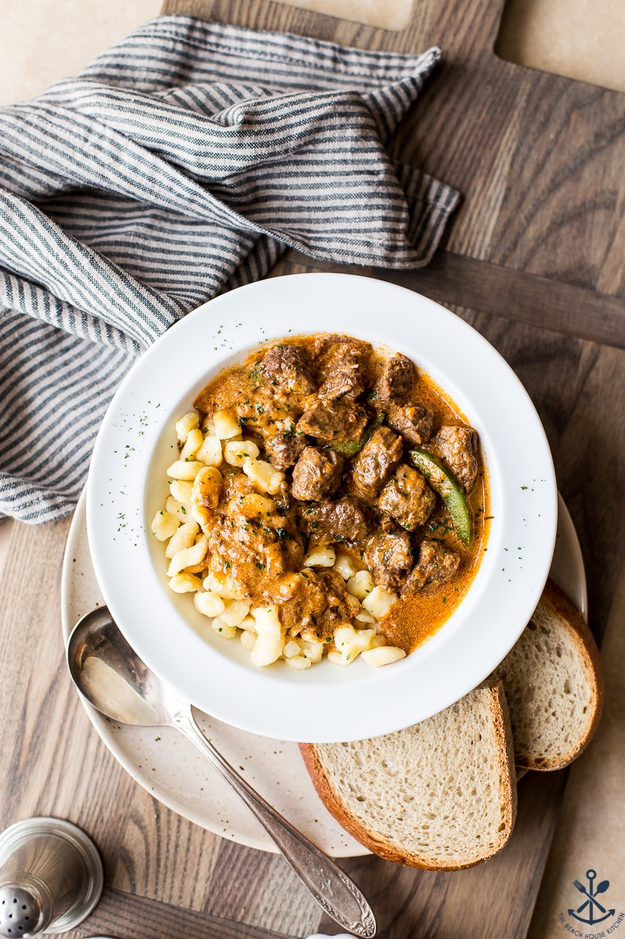 Overhead photo of Hungarian beef goulash in a white bowl on a wooden board