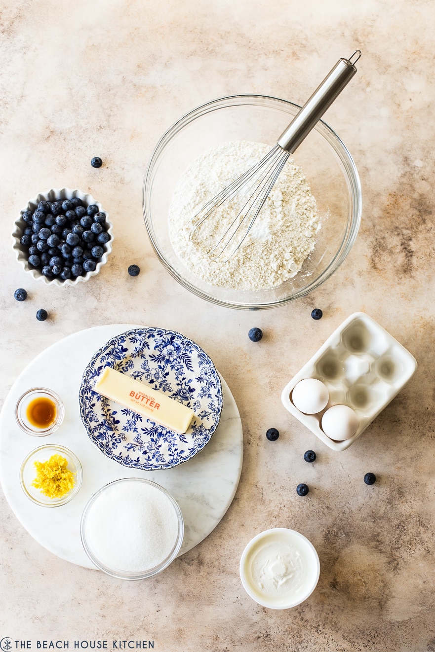 Overhead photo of ingredients for Blueberry Lemon Loaf in bowls of different sizes on a tan background