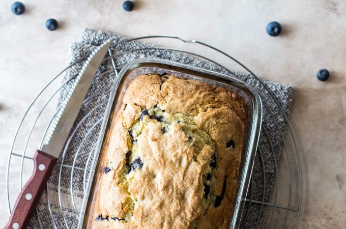 Overhead photo of blueberry lemon loaf on a round wire rack with a bowl of blueberries and a cup of coffee