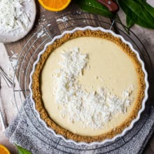 Overhead photo of an orange cream tart on a round wire rack surrounded by halved oranges