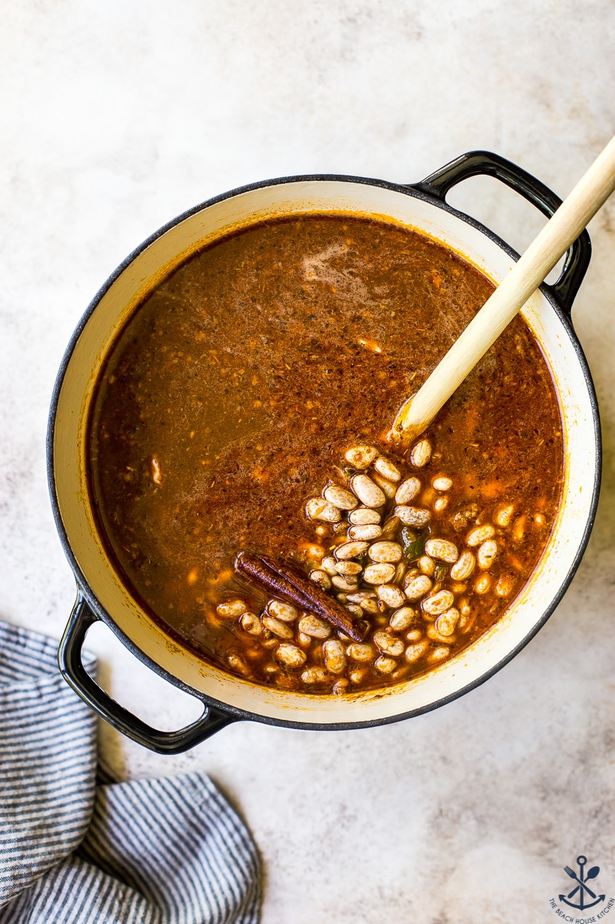 Overhead photo of pot filled with pinto beans, broth and a cinnamon stick
