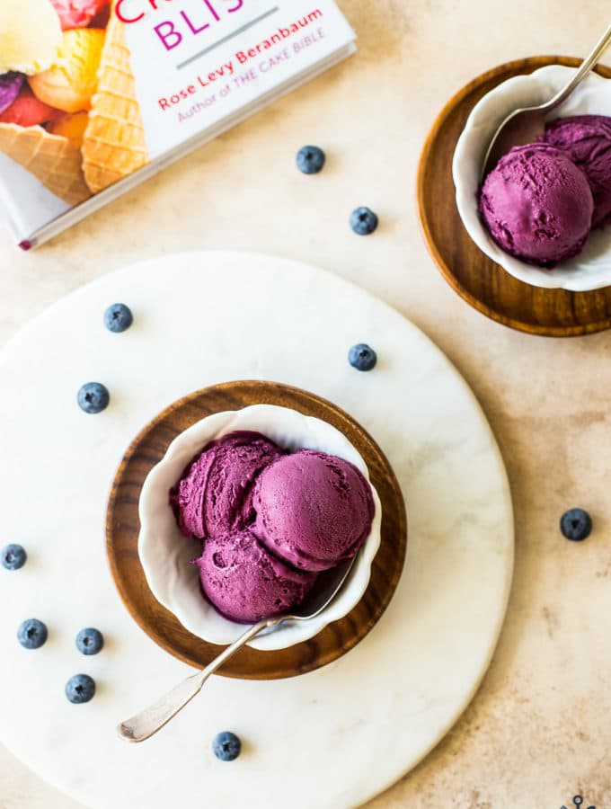 Overhead photo of white dishle board filled with dark purple blueberry ice cream on round marb