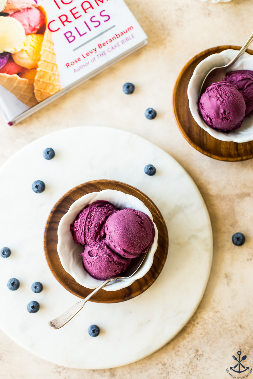 Overhead photo of white dishle board filled with dark purple blueberry ice cream on round marb
