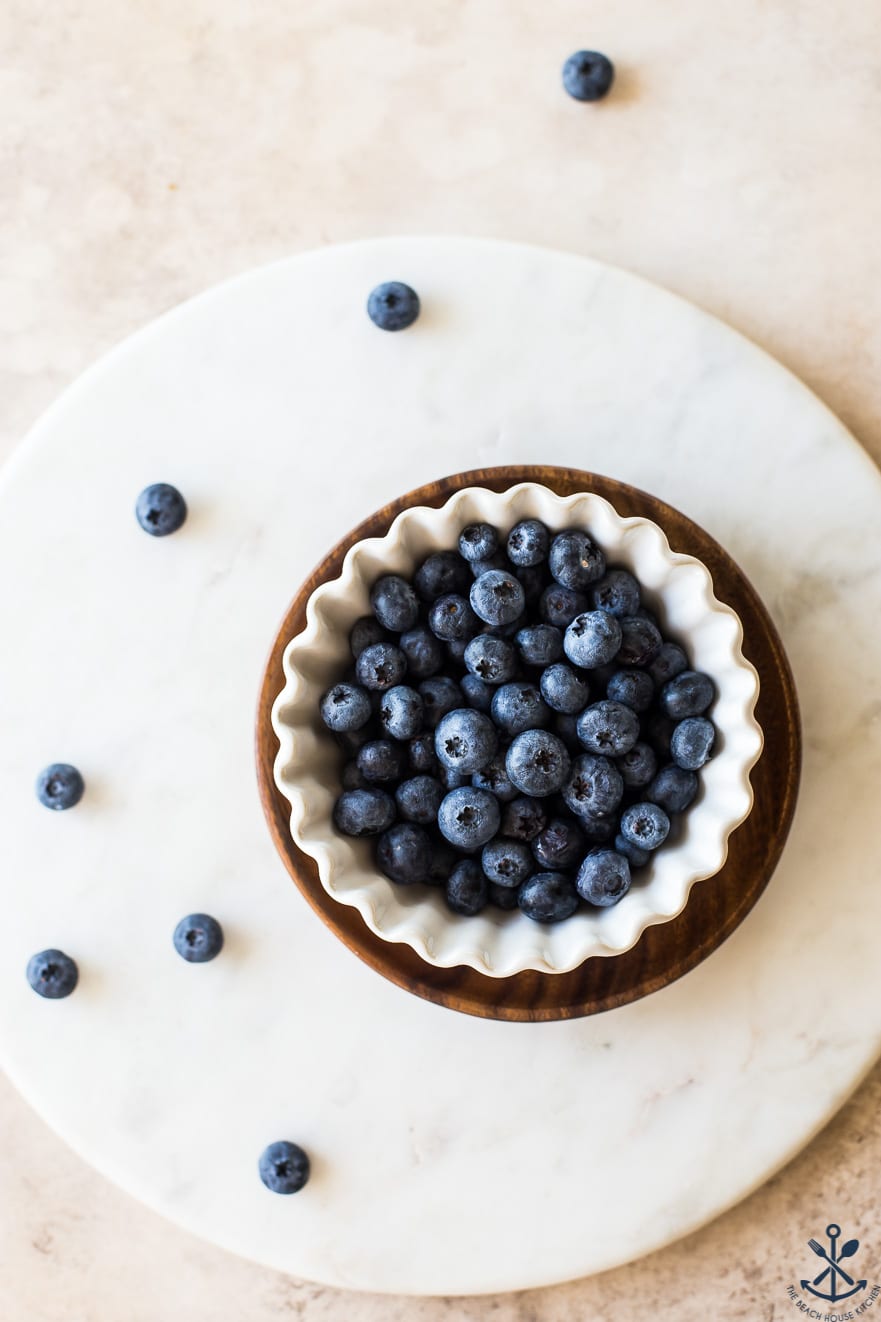 Overhead photo of blueberries in a white scalloped bowl on a round marble board