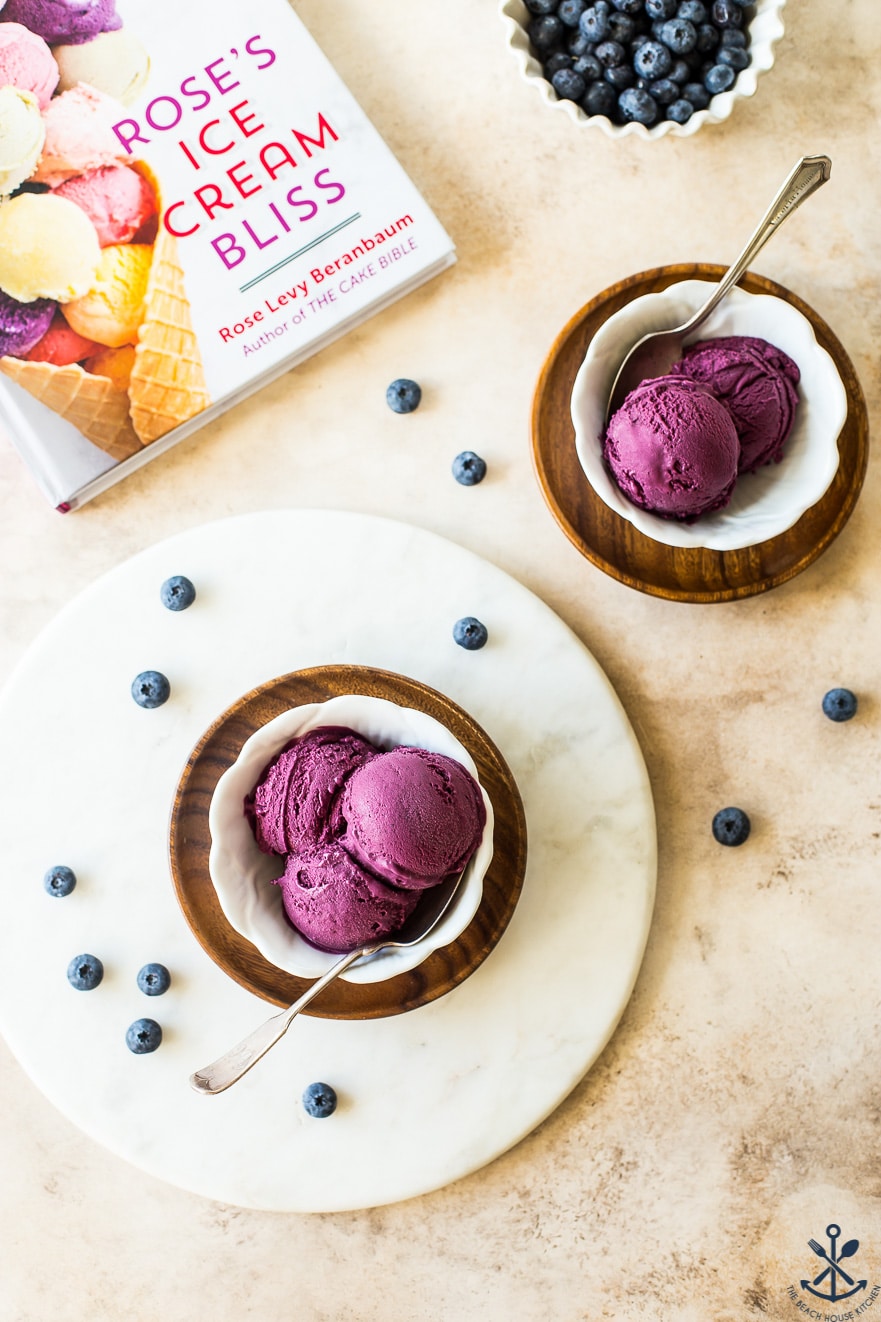 Overhead photo of blueberry ice cream in two bowls, one a round marble board