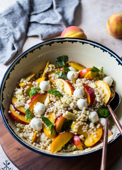 Peach Corn Caprese Couscous Salad in a bowl on a wooden board