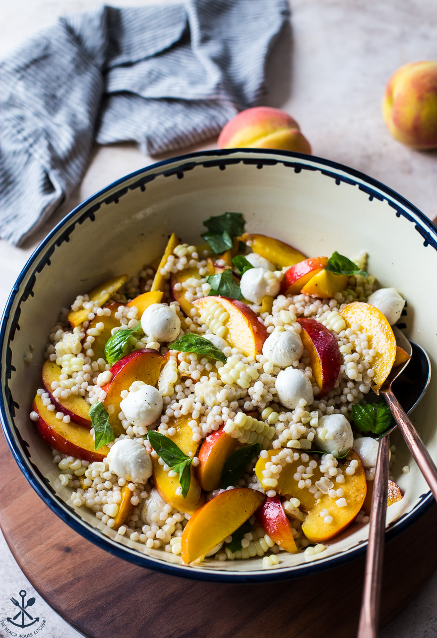 Peach Corn Caprese Couscous Salad in a bowl on a wooden board