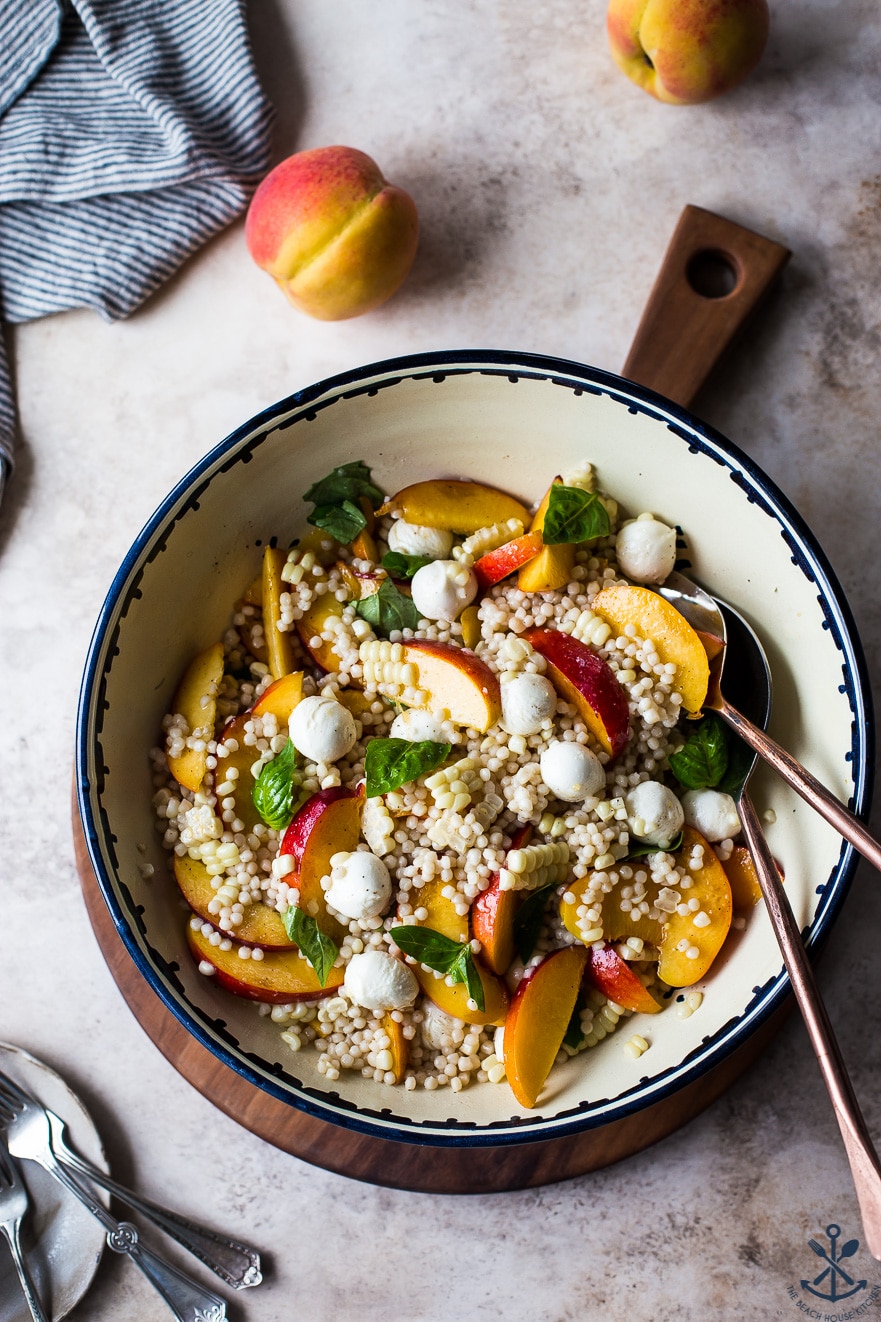 Peach Corn Caprese Couscous Salad in a bowl on a round wooden board