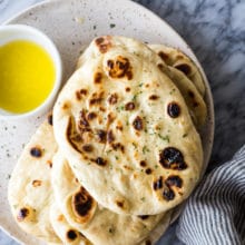 Overhead photo of homemade naan bread on a plate with a bowl of melted butter