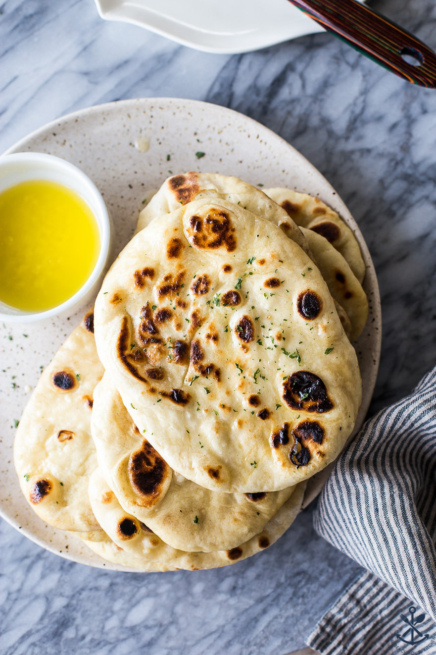 Overhead photo of naan bread on a plate with a bowl of melted garlic butter