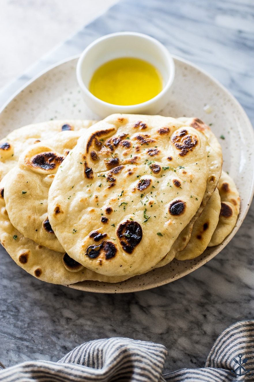 Homemade naan bread on a plate with a bowl of melted garlic butter