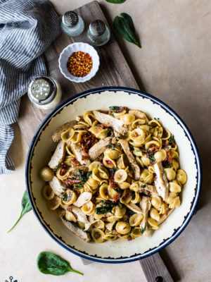 Chicken Pasta with Sun-Dried Tomato Bacon Cream Sauce in a large bowl on a wooden board
