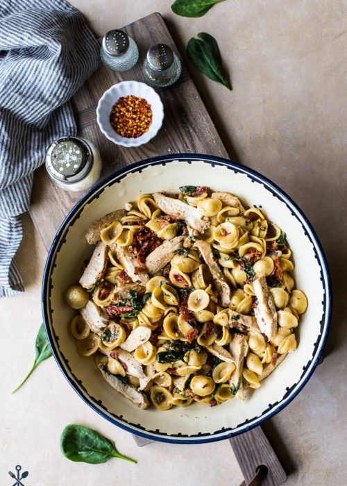 Chicken Pasta with Sun-Dried Tomato Bacon Cream Sauce in a large bowl on a wooden board