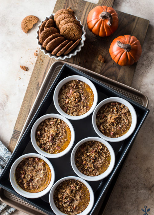 Pumpkin Custards with Gingersnap Crumbles in white ramekins on a wooden board