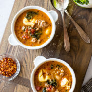 Overhead photo of two white bowls on a wooden board filled with tomato tortellini stew