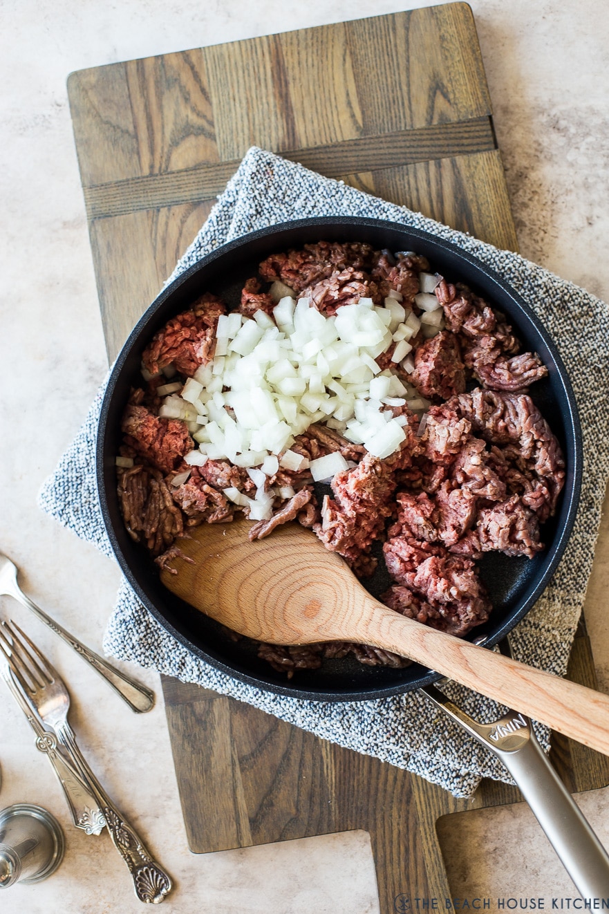 Pre-cooked ground beef topped with onions in a skillet carefully presented on a wooden board