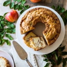 Overhead photo of Jewish Apple Cake on a white cake plate surrounded by apples and greens