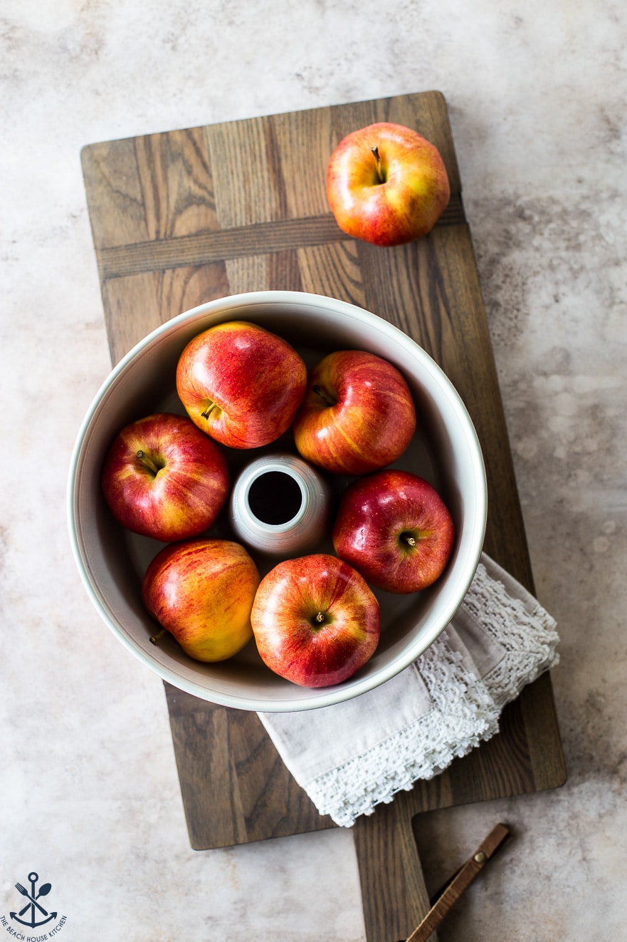 Overhead photo of red apples in a tube pan on a wooden board looking extra colorful