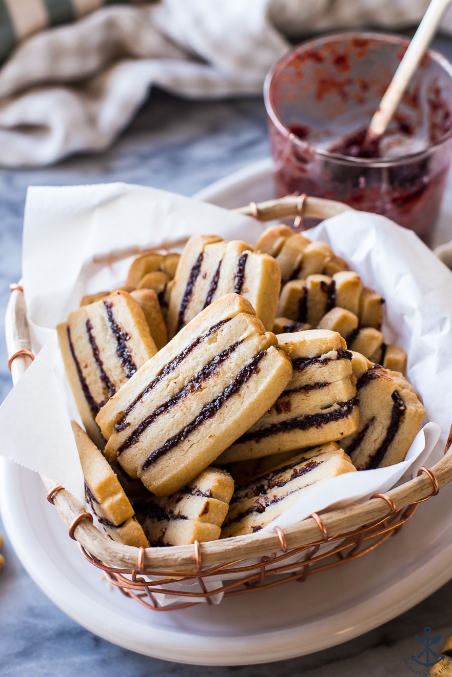 A basket filled with cherry ribbon butter cookies with a glass jar of jam in the background