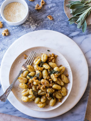 Overhead photo of plate of Gnocchi with Walnut Brown Butter Sage Sauce on a marble board with sage leaves