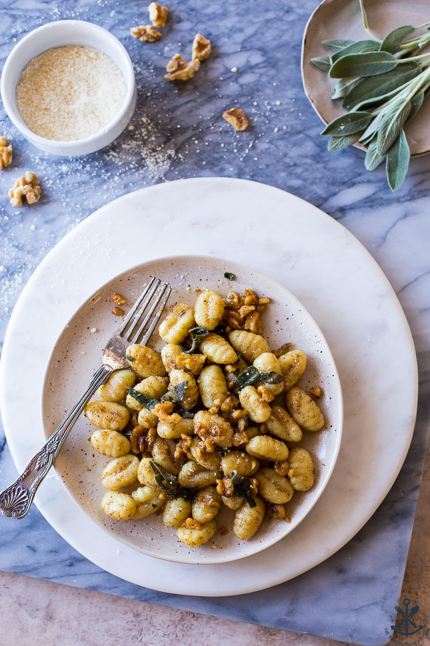Overhead photo of a plate of Gnocchi with Walnut Brown Butter Sage Sauce on a marble board with sage leaves on a plate