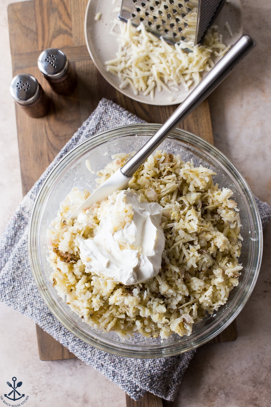 Overhead photo of glass bowl filled with shredded potatoes and sour cream with a spatula