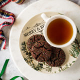 Overhead photo of a plate of 3 chewy chocolate gingersnap cookies with a cup of tea