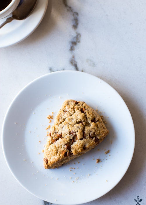 A cinnamon chip scones on a white plate with a cup of coffee off to the side.