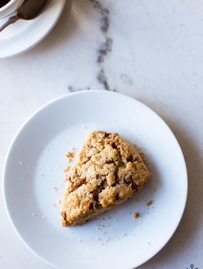 A cinnamon chip scones on a white plate with a cup of coffee off to the side.