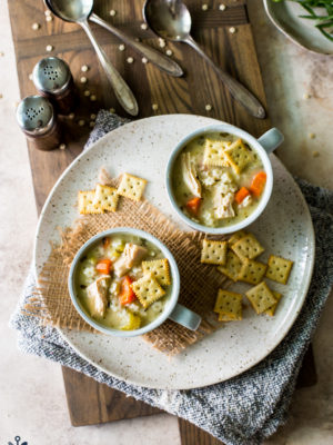 Overhead photo of two mugs filled with chicken soup with stars on a plate with saltine crackers