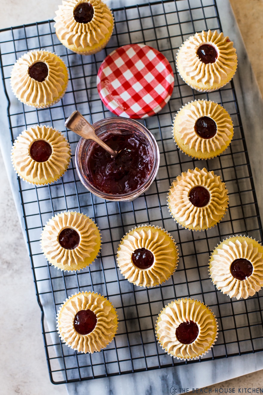 Overhead photo of Peanut Butter and Jelly Cupcakes on a wire rack with a jar of preserves