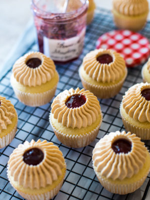 Peanut Butter and Jelly Cupcakes on a wire rack with a jar of strawberry preserves