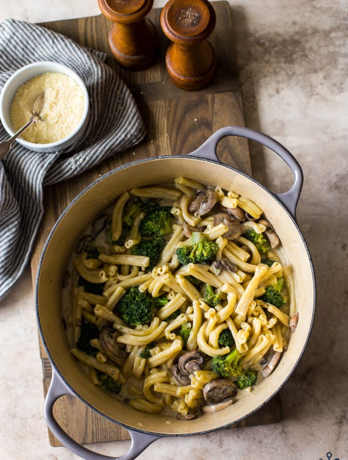 Overhead photo of a pot filled with Creamy Garlic Broccoli Mushroom Pasta on a wooden board