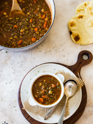 Overhead photo of a bowl of lentil soup on a round white board with a pot of soup in the background