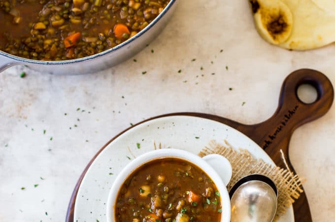 Overhead photo of a bowl of lentil soup on a round white board with a pot of soup in the background