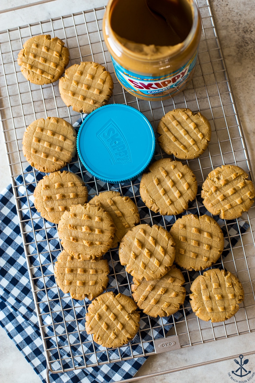 Overhead photo of peanut butter cookies on a wire rack with a jar of peanut butter and a blue lid