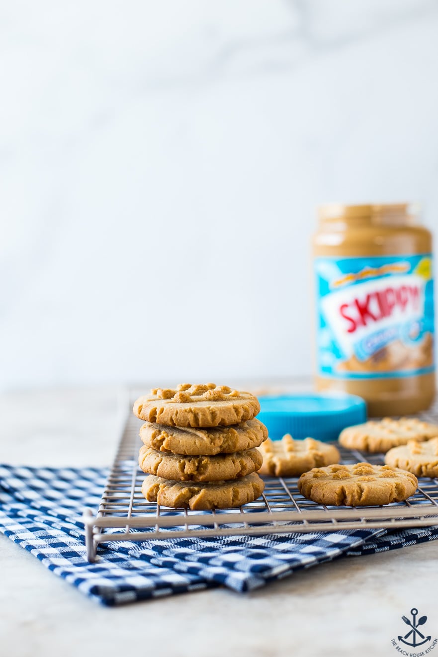 A stack of 4 peanut butter cookies on a wire rack with a jar of peanut butter in the background