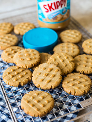 Peanut butter cookies on a wire rack with a jar of Skippy peanut butter and a blue lid