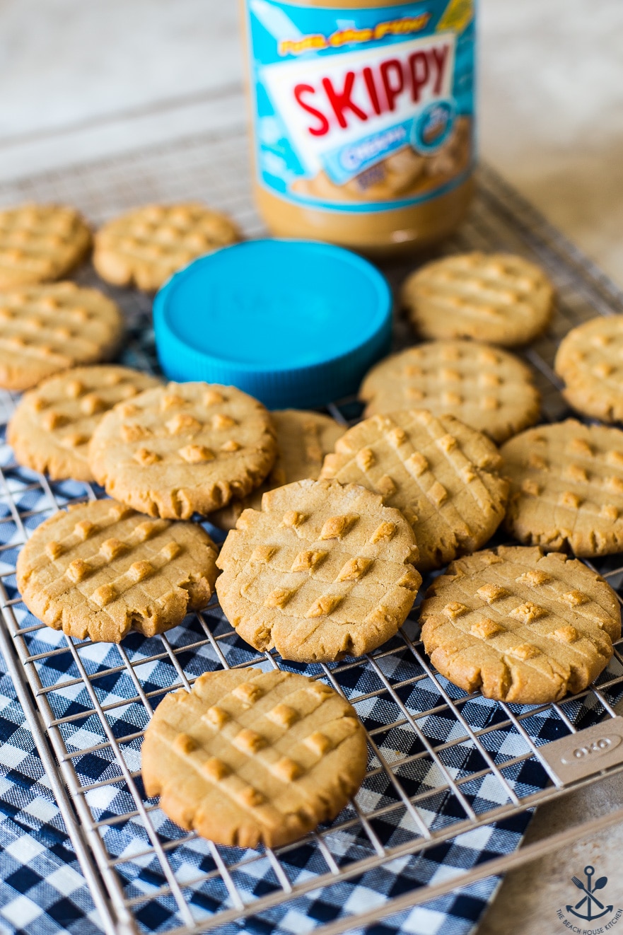 Peanut butter cookies on a wire rack with a jar of Skippy peanut butter and a blue lid